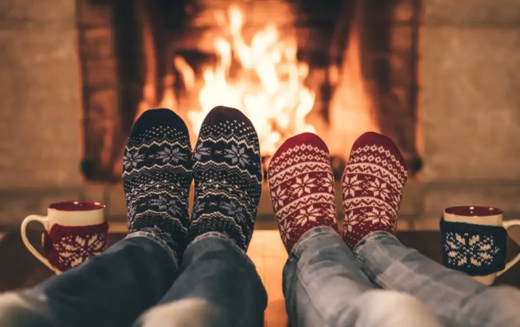2 sets of feet wearing socks in front of roaring fireplace